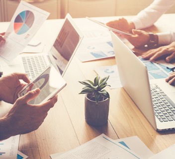 Photo: Individuals sitting around a desk access essential communications, such as bills and statements, different ways, including on paper and tablets